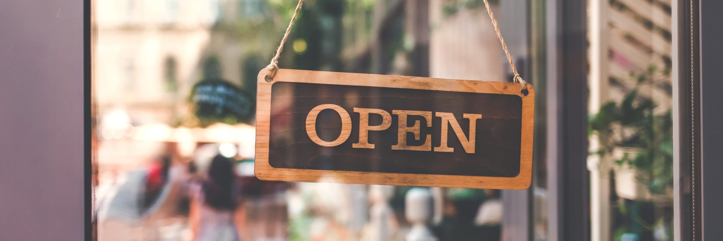 A wood-framed open sign hanging on a glass shop door