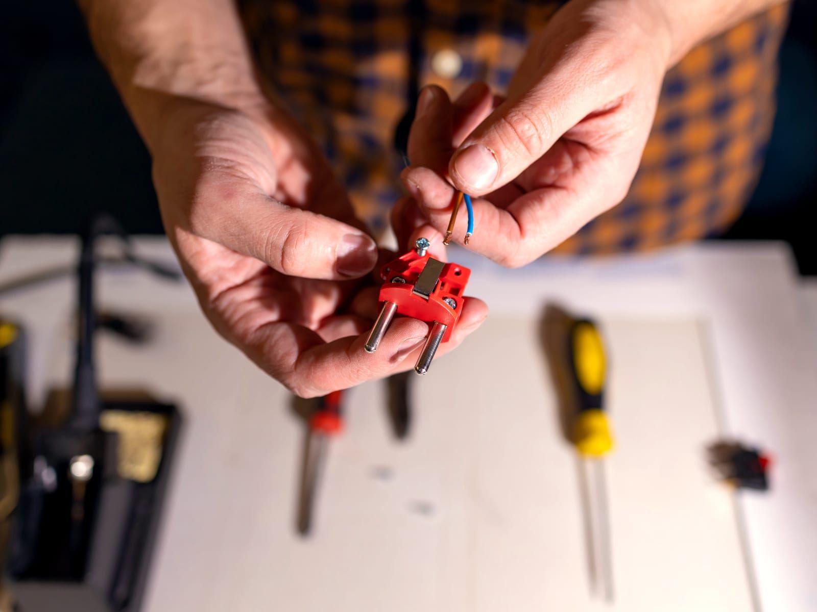 Hands connecting wiring inside an electrical plug over a workbench