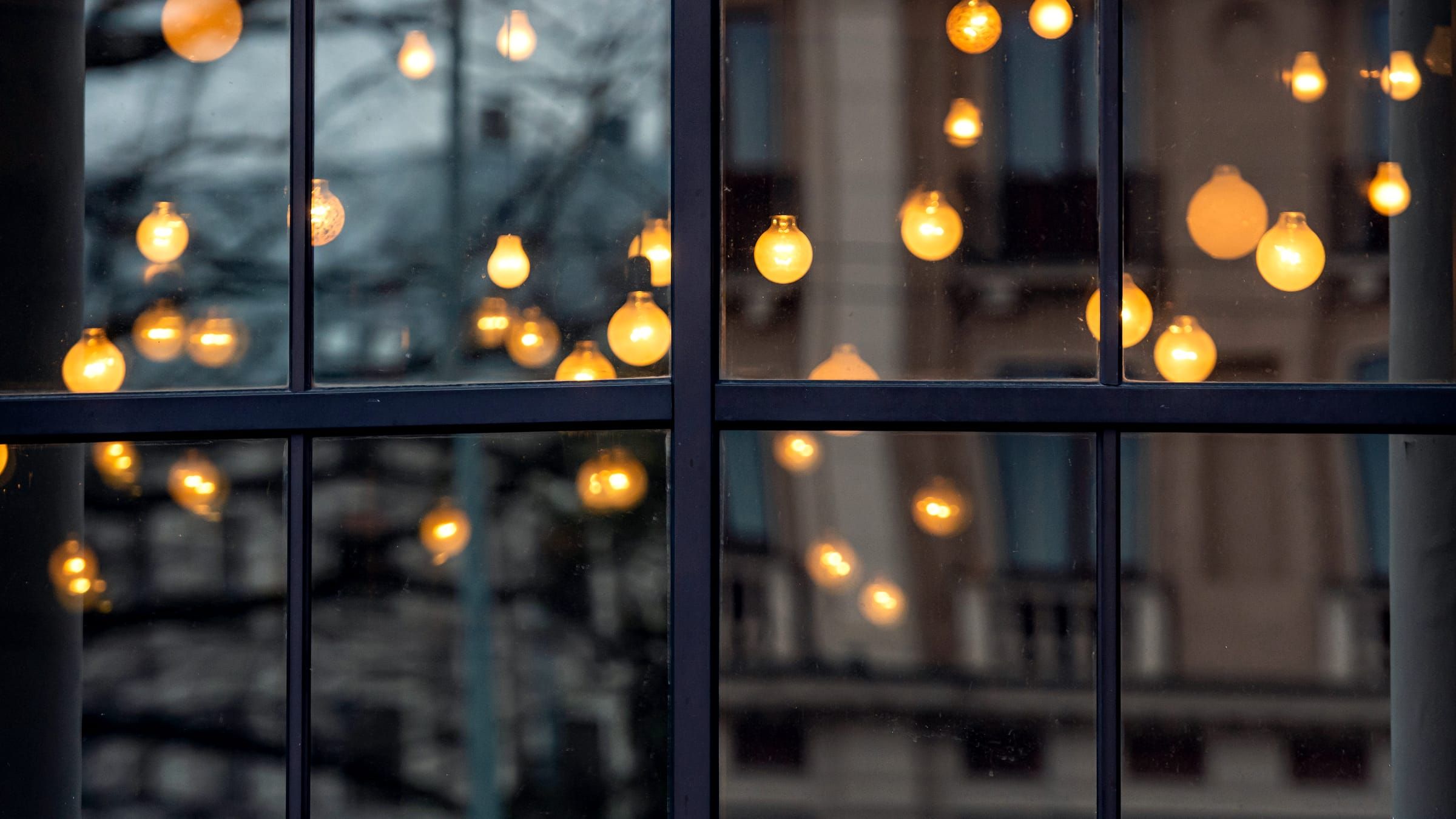 Warm bare lightbulbs glowing behind a paned shop window at dusk