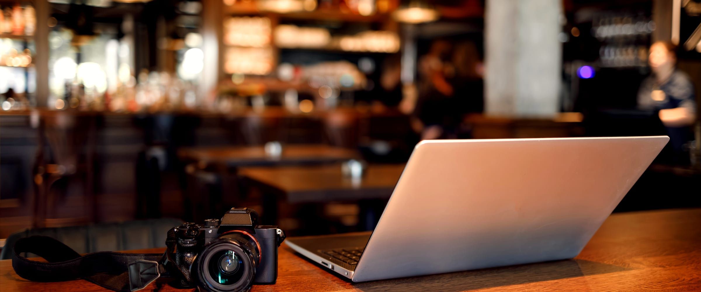 A camera and an open laptop side by side on a wooden table