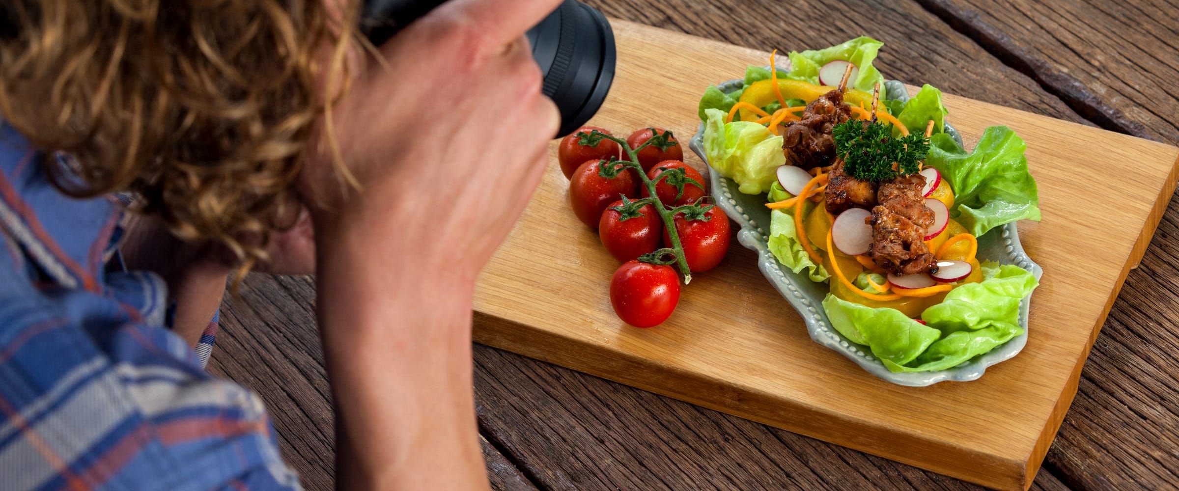 Over the shoulder of a photographer shooting plates of food on a timber table